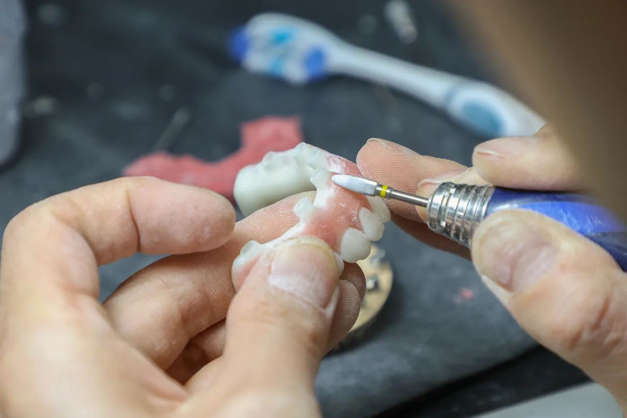 A technician's hands finishing a denture at the bench in Luminous Dental Ceramics, the Enhanced Dental Studios lab in Southport.
