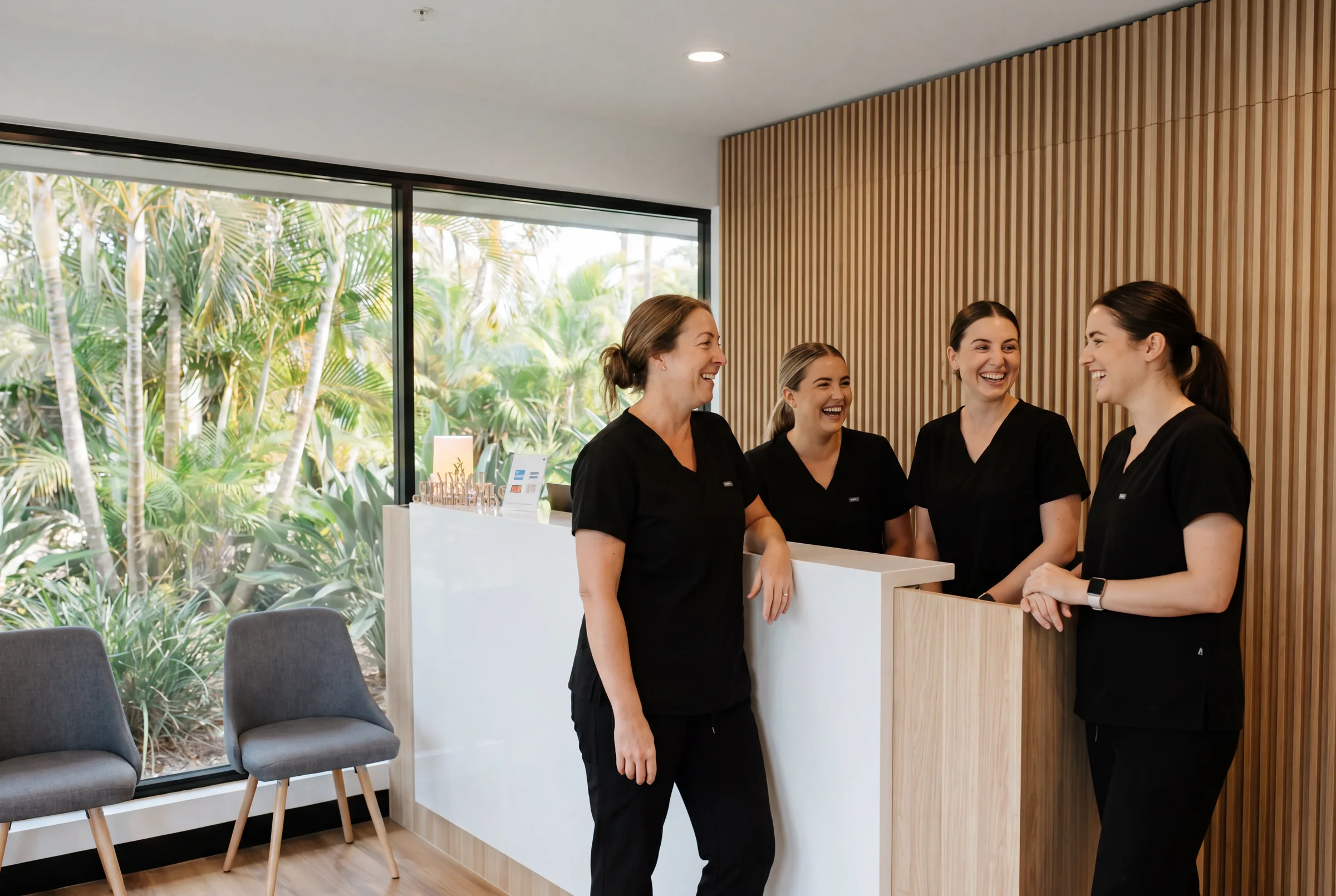 An Enhanced Dental Studios clinic team sitting together in their bright, window-lit reception.