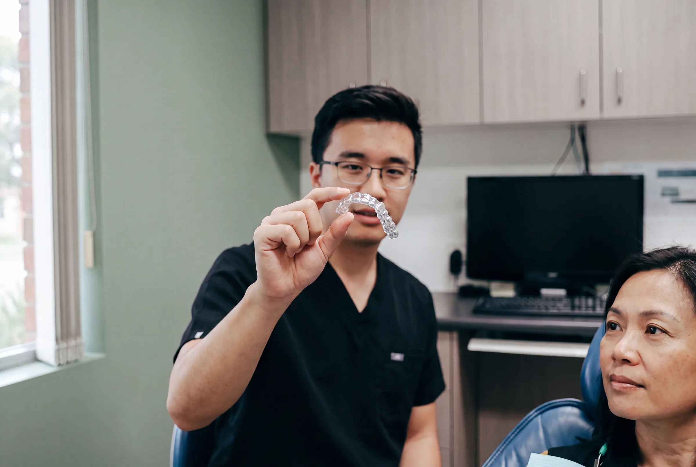 A patient holding a clear Invisalign aligner while discussing their plan at Enhanced Dental Studios.