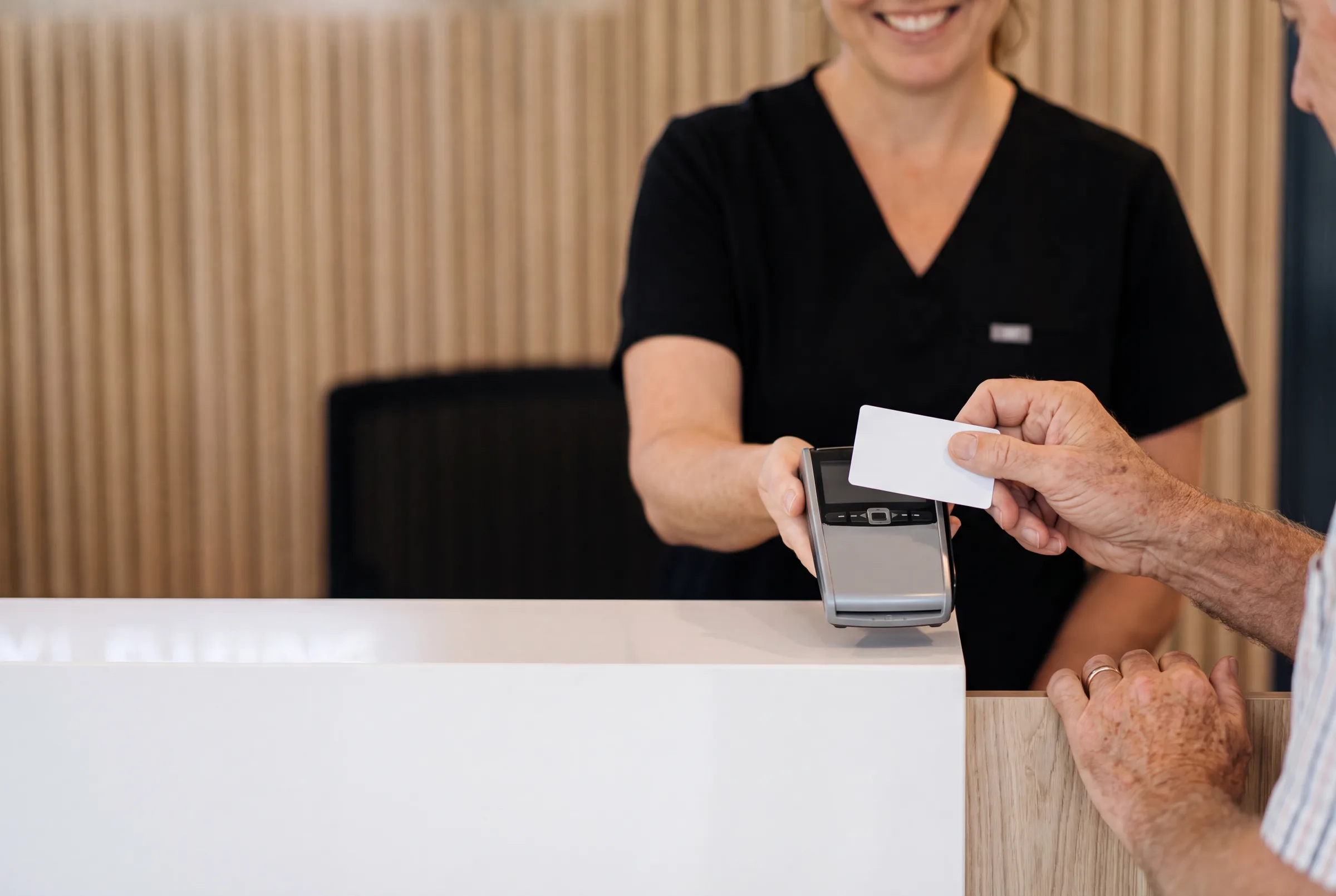 An Enhanced Dental Studios patient tapping their health fund card at reception to claim on the spot.