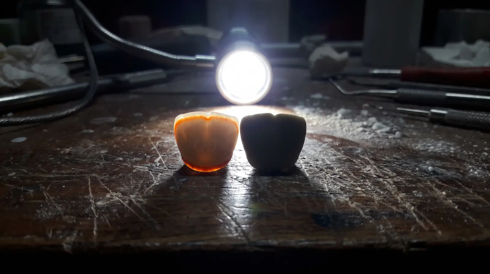 Two crowns on a workbench lit from behind. One glows warm where light passes through it. The other blocks the light completely and reads flat and dead.