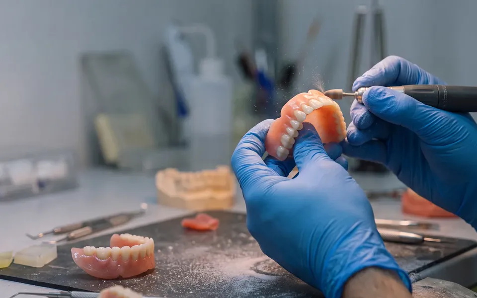 A denture being finished by hand under the lamp at the Enhanced Dental Studios lab.