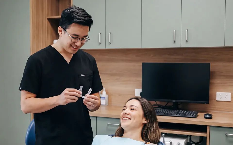 An Enhanced Dental Studios dentist preparing take-home whitening for a smiling patient.