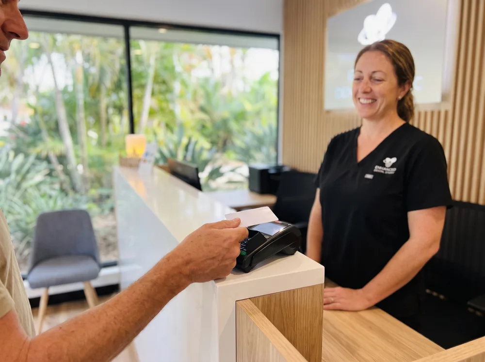 A patient tapping their health-fund card on the HICAPS terminal at the Enhanced Dental Studios front desk.