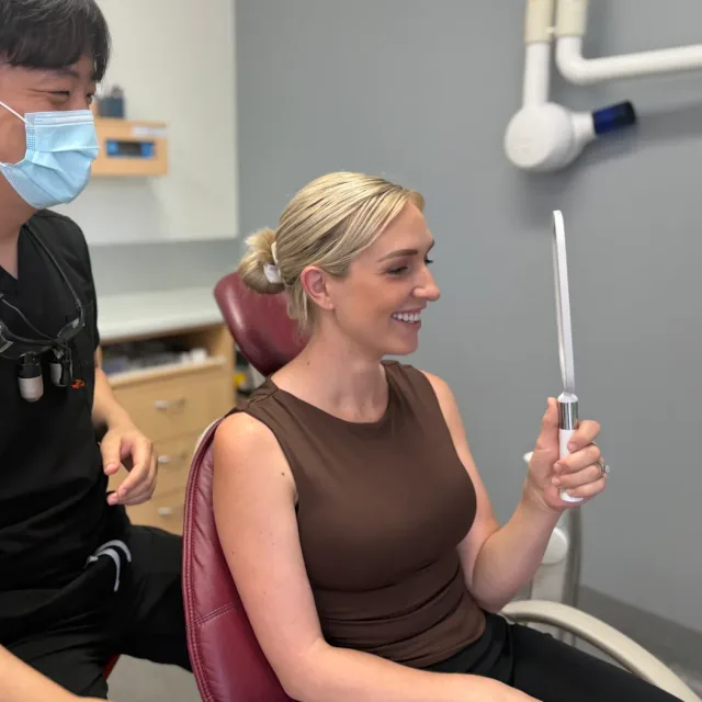 A patient checking her smile in a hand mirror during a gentle check-up.