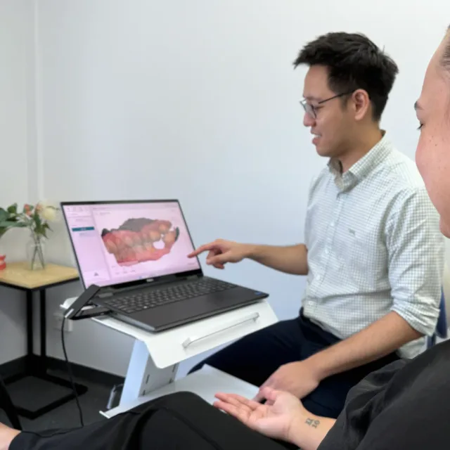 A dentist walking a patient through her 3D scan on a laptop.