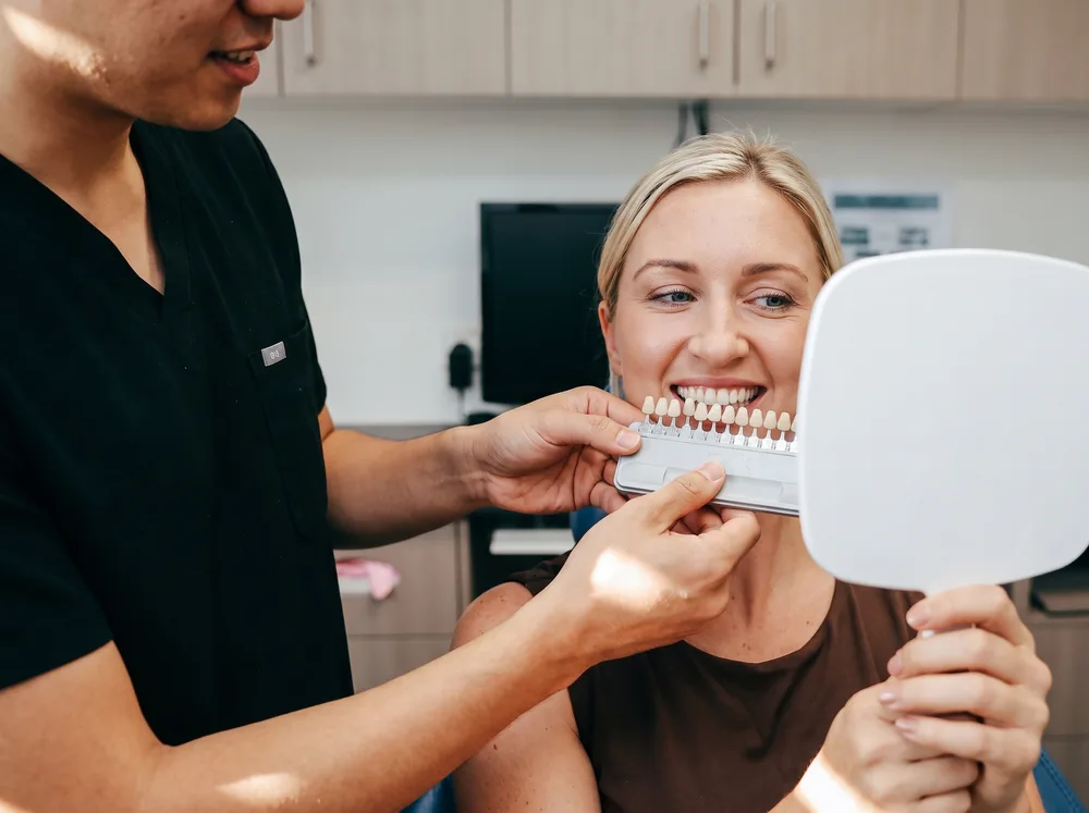 A shade guide held against a patient's smile at Enhanced Dental Studios.