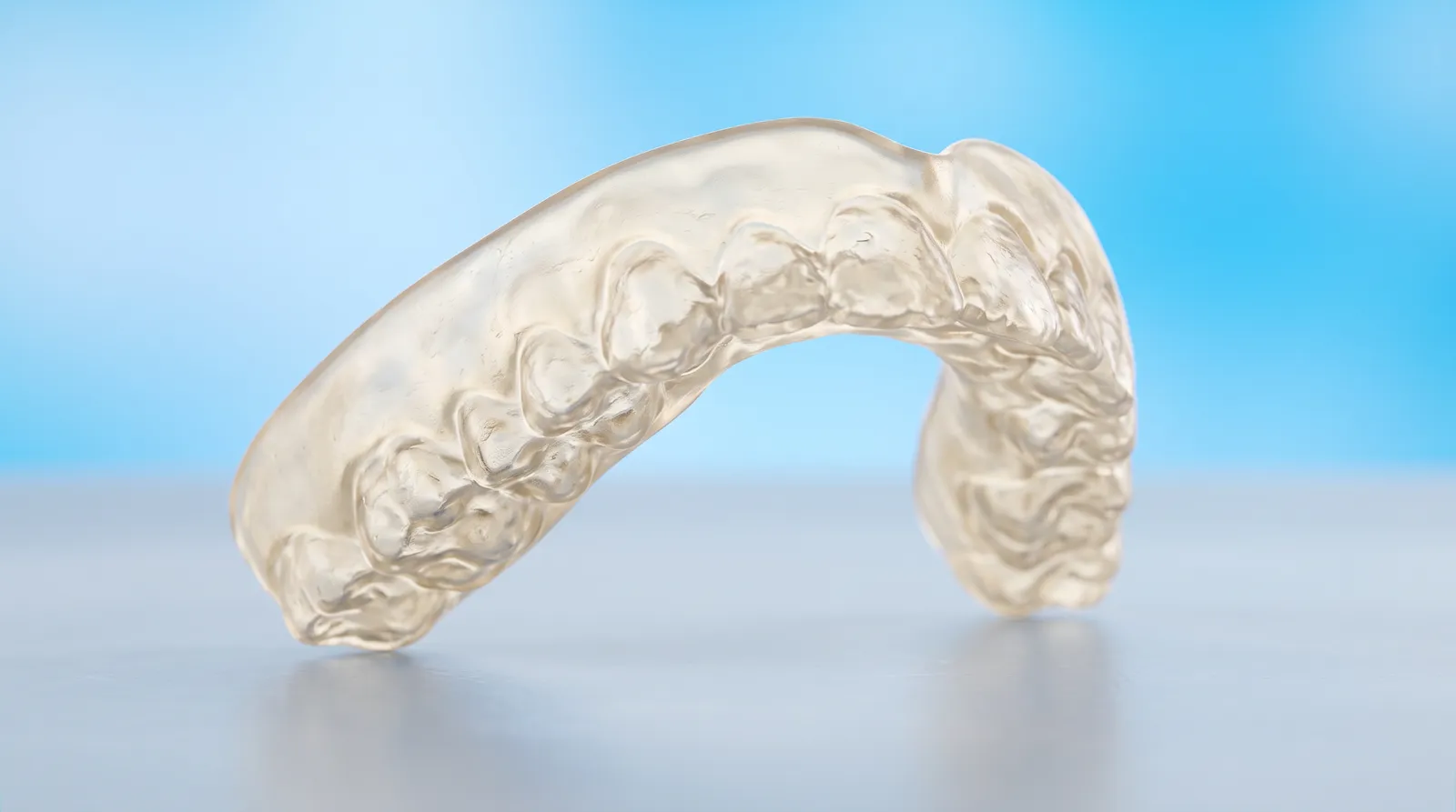 A thick clear mouthguard alone, its inner impressions lumpy and its arch shape twisted out of true